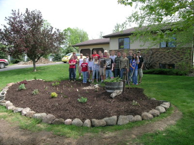 A group of people holding shovels behind a freshly planted garden